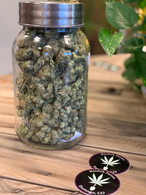 Glass jar full of marijuana with stickers on table.